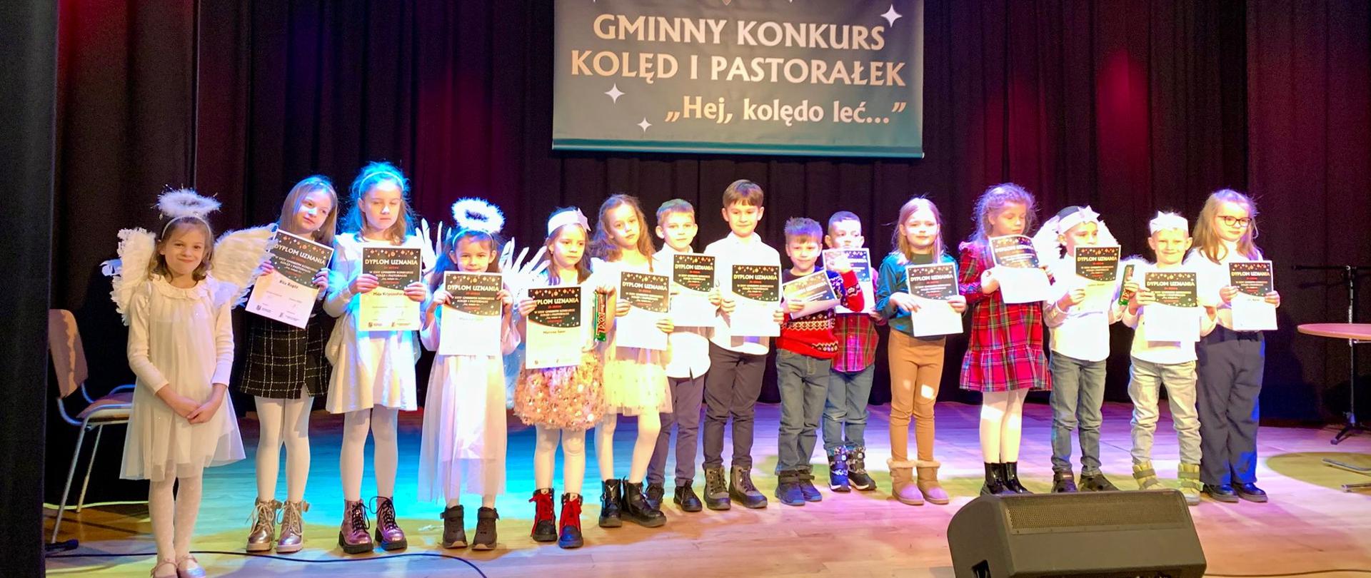 Uczniowie klas 0 - II stoją na scenie z dyplomami.