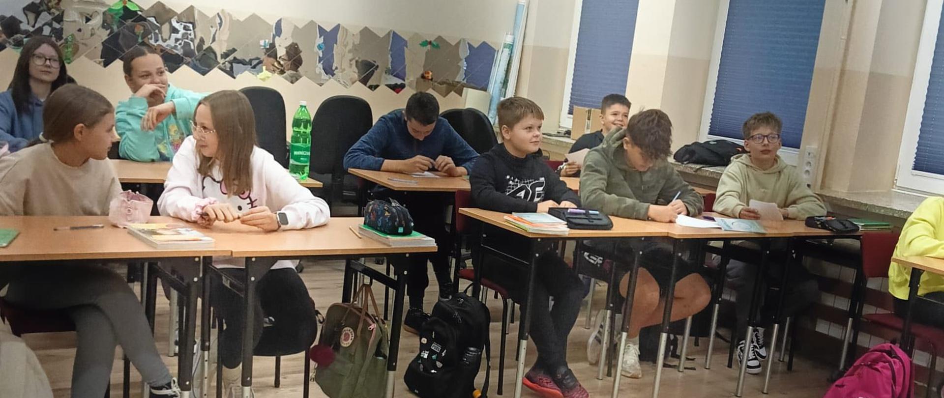Uczniowie klasy szóstej siedzą w ławkach szkolnych i wypełniają karty do głosowania