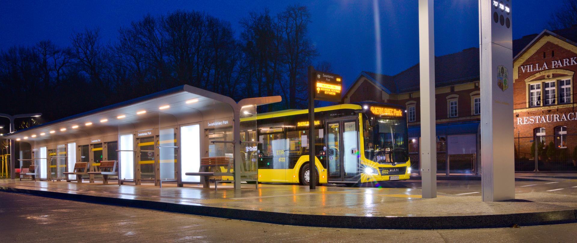 Oświetlone centrum przesiadkowe w Świerklańcu wieczorową porą. Na peronie żółty autobus.