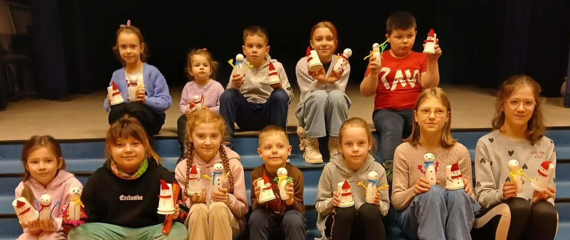 Zdjęcie przedstawiające na środku 12 dzieci siedzących na schodach sali Ośrodka Kultury w Grodzisku Dolnym