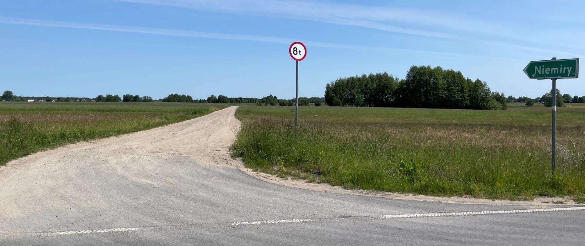 Droga żwirowa wśród łąk i pól. W prawej części zdjęcia znak w kształcie strzałki Niemiry ora zakaz wjazdu dla pojazdów powyżej 8t.