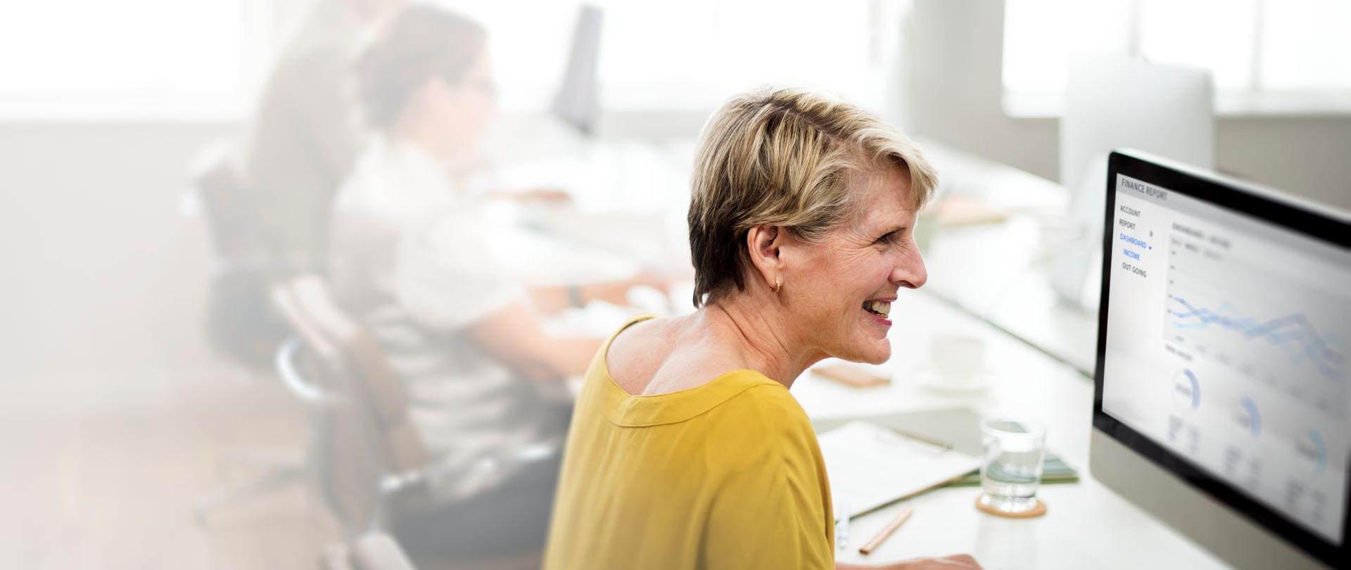 Starsza kobieta pracuje uśmiechnięta przy komputerze