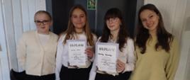Dziewczyny biało ciemnych strojach pozują do zdjęcia dwie w środku trzymają dyplomy