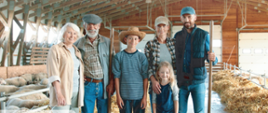 Grafika przedstawia sześcioosobową rodzinę rolników: od lewej babcia, dziadek, nastoletni chłopiec, mama, tata oraz kilkuletnia dziewczynka. Rodzina stoi w budynku gospodarczym, w tle widać owce i słomę.