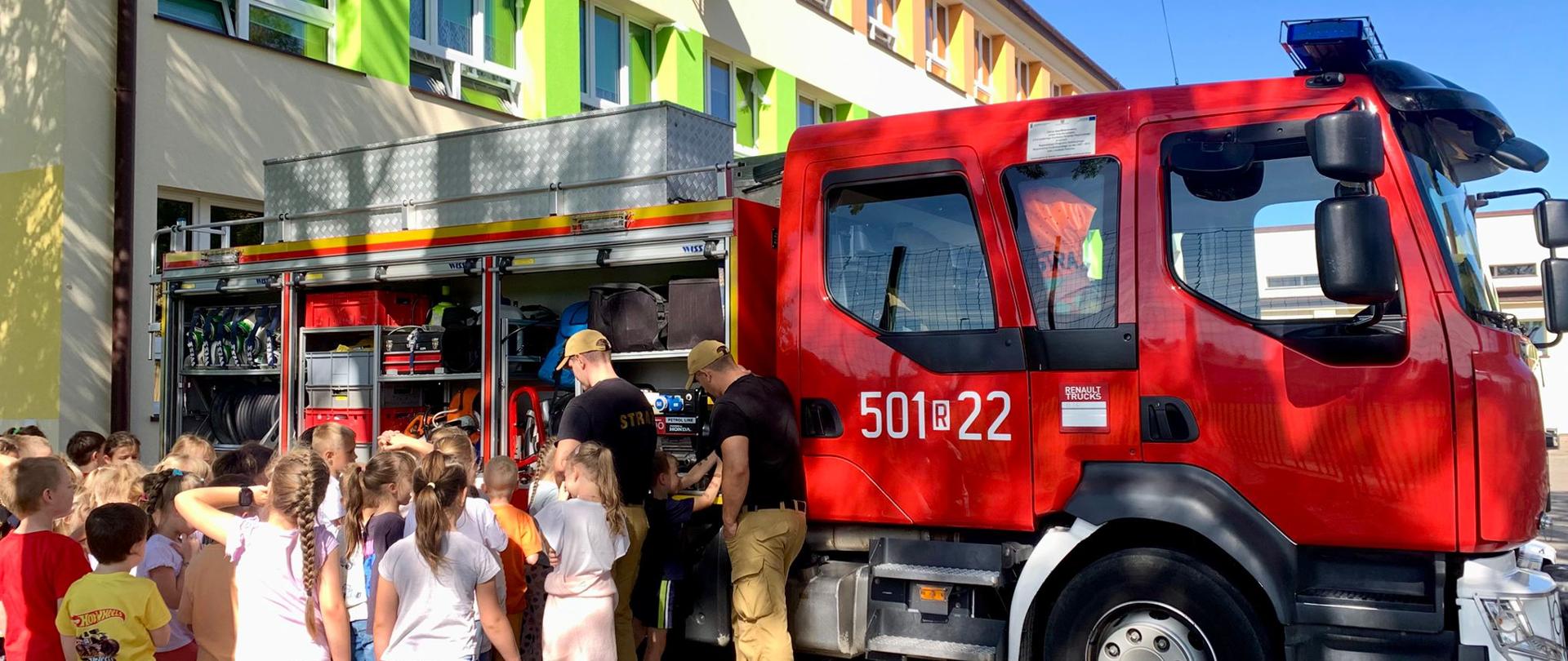 Strażacy przedstawiają wyposażenie wozu strażackiego uczniom z klas młodszych.