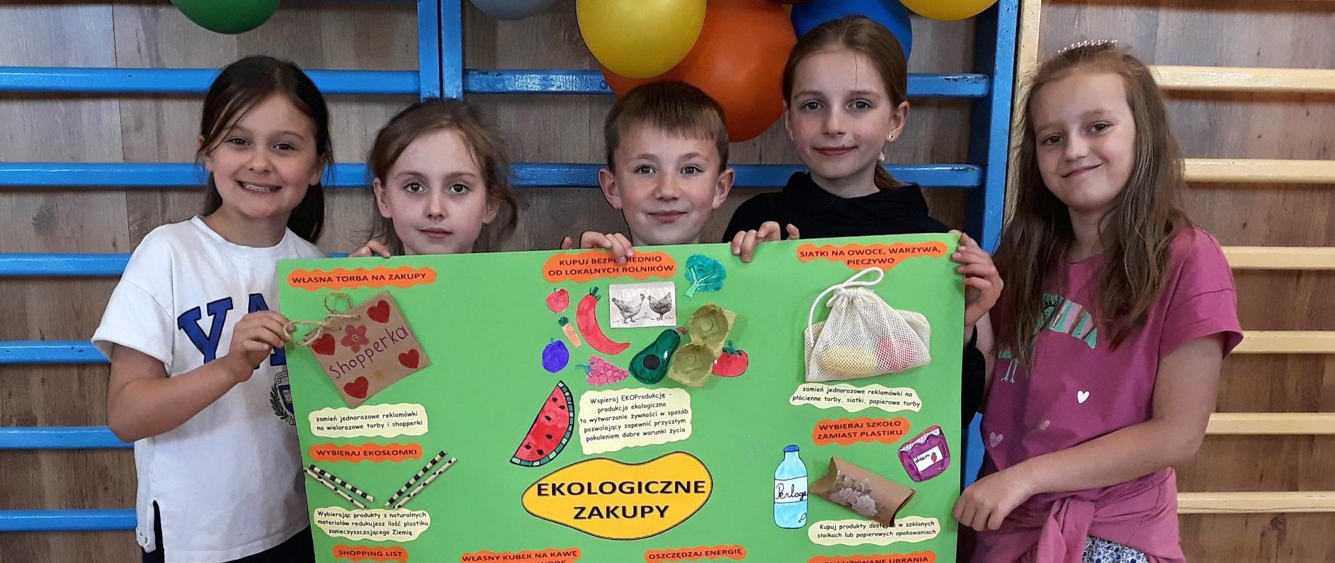 Pitka uczniów trzyma w rękach samodzielnie przygotowany plakat pt. "Ekologiczne zakupy"