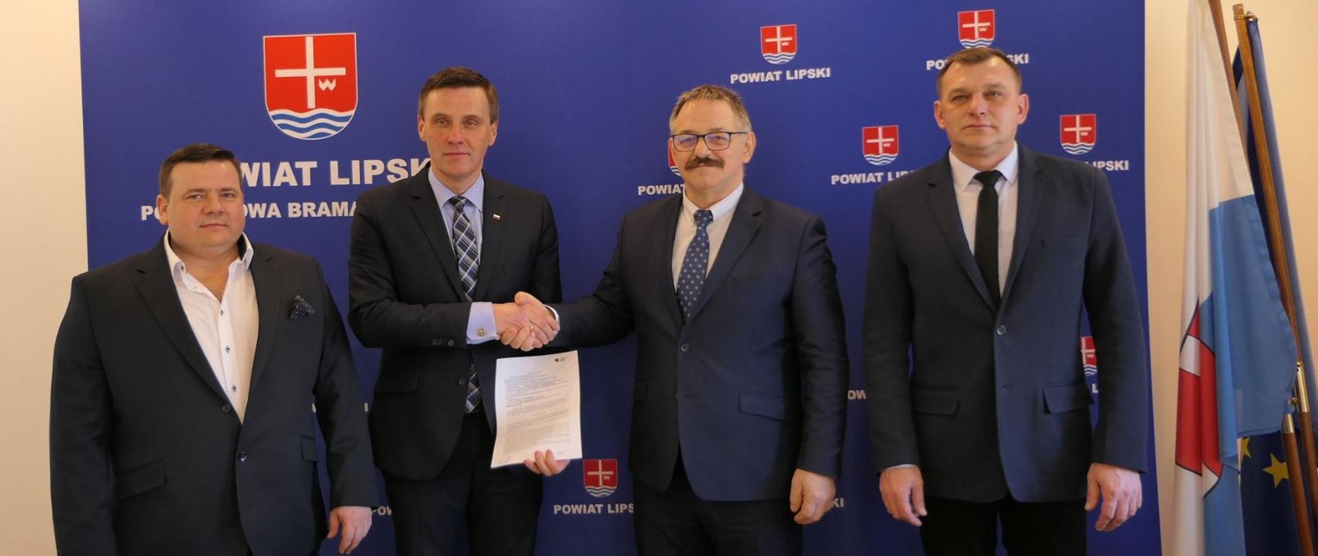 Przedstawiciele jednostek ujętych w umowie prezentują podpisaną umowę. Starosta lipski oraz Wójt Gminy Ciepielów podają sobie dłoń. W tle granatowa ścianka z Herbem powiatu i napisem Powiat Lipski Południowa Brama Mazowsza.