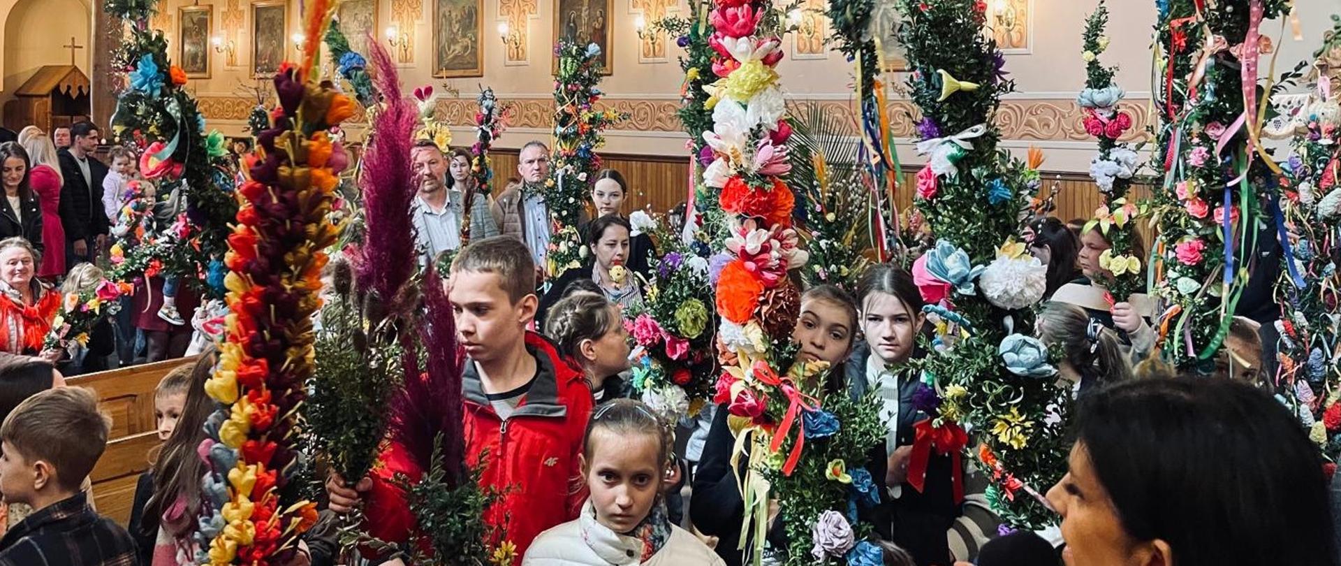 Konkurs palm wielkanocnych w Kościele w Rabie Wyżnej. Dzieci z kolorowymi palmami stoją przed ołtarzem a Pani Ania organizator przemawia do mikrofonu. 