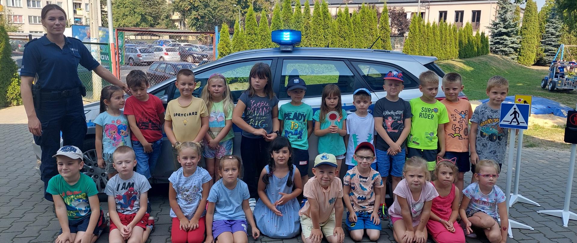 Grupa dzieci i 1 policjantka przed radiowozem