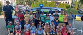 Grupa dzieci i 1 policjantka przed radiowozem