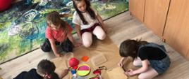 Zajęcia matematyczne - grupa dzieci siedzi na podłodze, przy materiałach do pisania