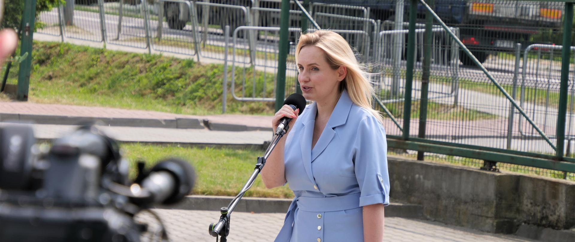 Zdjęcie przedstawia jedną osobę stojącą na zewnątrz przy mikrofonie