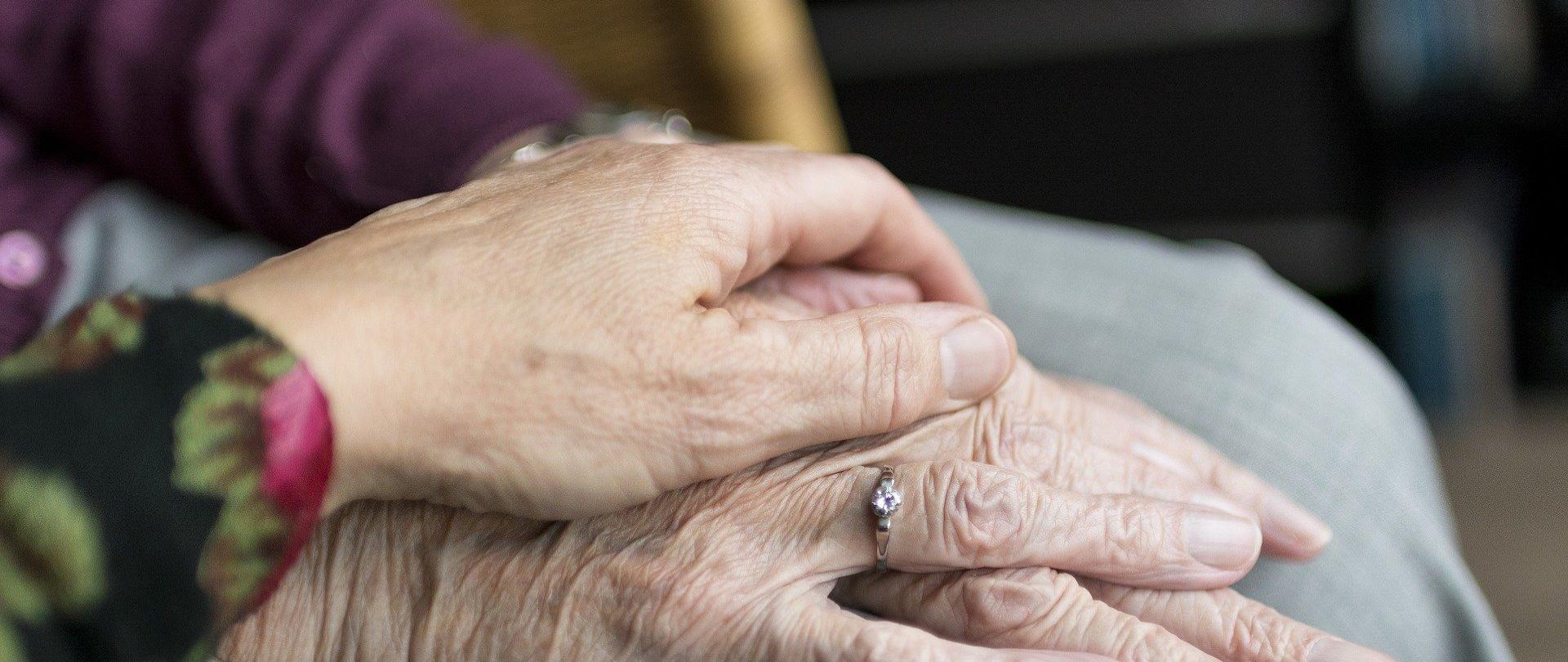 dłonie seniorki, przykryte dłonią młodszej osoby, symbol wsparcia i pomocy