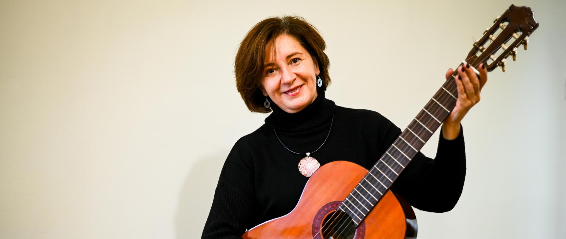 Uśmiechnięta kobieta z gitarą akustyczną.