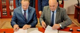 Zdjęcie uwiecznia moment podpisania umowy pomiędzy Zespołem Szkół Powiatowych w Przasnyszu a Politechniką Warszawską na zawiązanie współpracy oraz utworzenie klasy o profilu technik mechanik lotniczy. Na fotografii widać podpisujących umowę od lewej: Prof. dr hab. inż. Janusz Frączak, Dziekan Wydziału Mechanicznego Energetyki i Lotnictwa Politechniki Warszawskiej oraz Andrzej Brocki, dyrektor Zespołu Szkół Powiatowych im. mjra Henryka Sucharskiego w Przasnyszu. Nad nimi stoją od lewej: prof. dr. hab. inż. Roberta Głębockiego, profesora z Zakładu Mechaniki Instytutu Techniki Lotniczej i Mechaniki Stosowanej Politechniki Warszawskiej oraz Starosta Powiatu Przasnyskiego Krzysztof Bieńkowski.