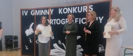 Maja w szarych spodniach, białej koszuli stoi z dyplom i ze statuetką stoi obok jury na sali gimnastycznej.