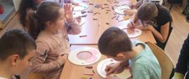 Uczniowie przy stoliku na drewniane krążki ozdabiają we wzory kwiatowe