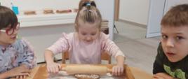 Wspólne pieczenie pierniczków - dzieci siedzą przy stole i wykonują czynności związane z przygotowaniem ciasteczek. Pozują przy tym do zdjęć