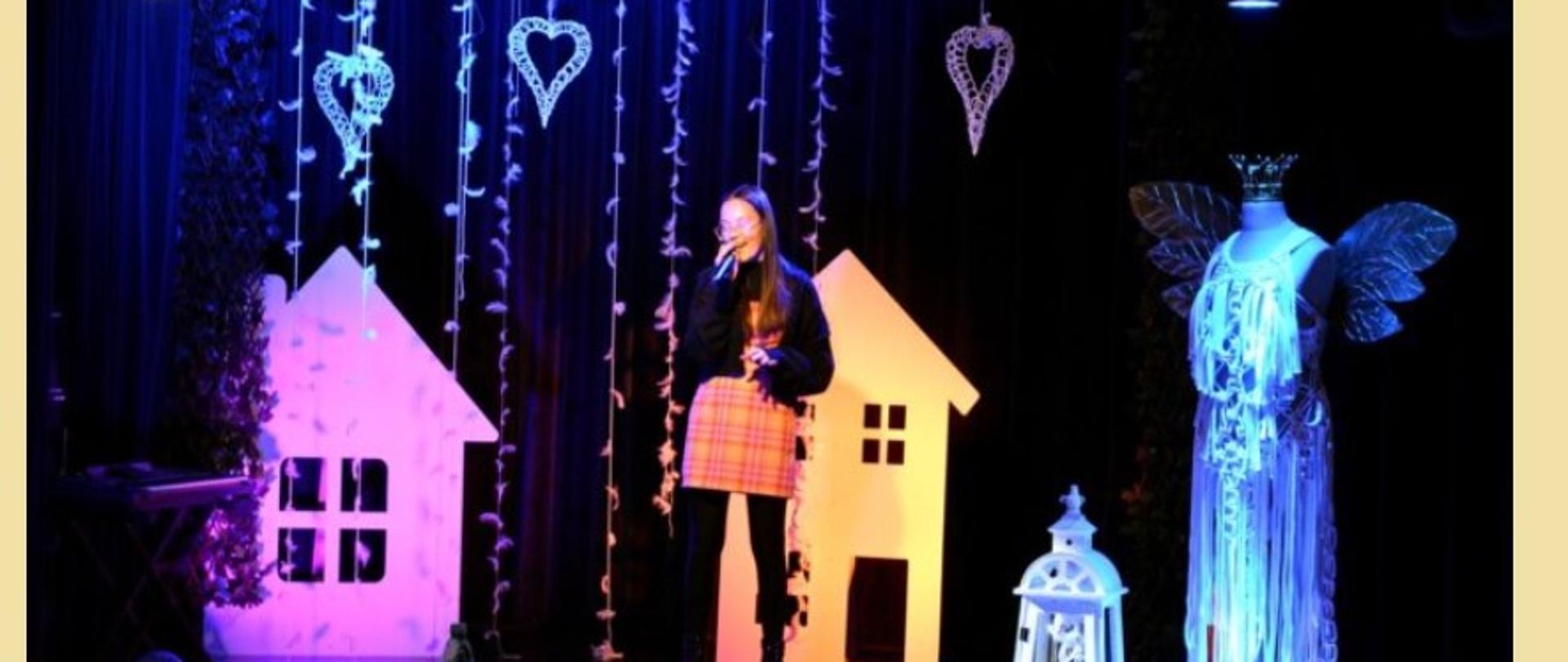 Wyróżniona uczennica śpiewa nagrodzoną piosenkę na tle dekoracji przedstawiającej kolorowe domki