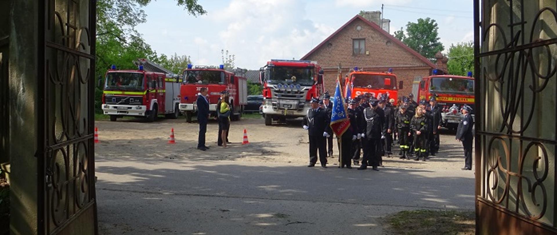 na tle samochodów strażackich kolumna strażaków ze sztandarem