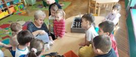 Dzieci przygotowują ogródek - stoją przy stole, na którym stoją donice i nasiona. Rozpoczyna się akcja sadzenie