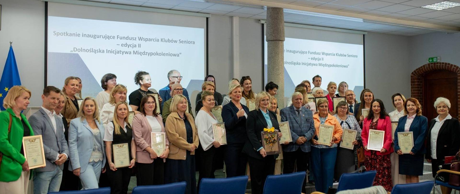 Grupa osób trzymająca w dłoniach dyplomy w ramkach