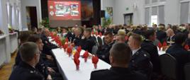Sala wypełniona umundurowanymi strażakami OSP i PSP siedzącymi przy długich stołach podczas oficjalnej odprawy operacyjnej w Wietrzychowicach.
