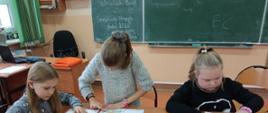 zdjęcie przedstawia dzieci w sali lekcyjnej, kolorujące kartki