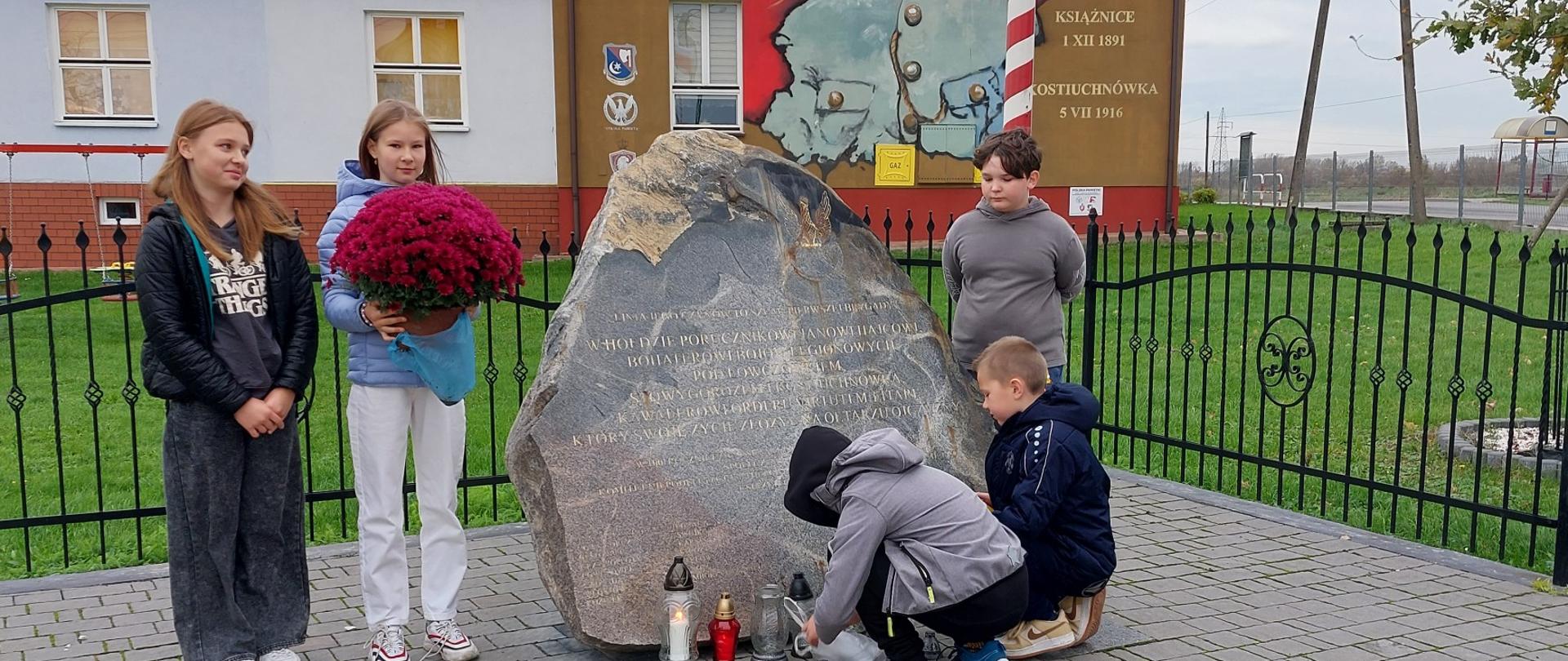 Uczniowie klasy V i VI na miejscu pamięci Jana Hajca składają chryzantemę i zapalają znicze.