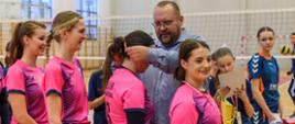 Fotografia na hali sportowej cztery zawodniczki w różowych koszulkach, pierwsza trzyma puchar, kolejnej przewodniczący Rady Powiatu Sokołowskiego zakłada medal, dwie pozostałe czekają w kolejce.