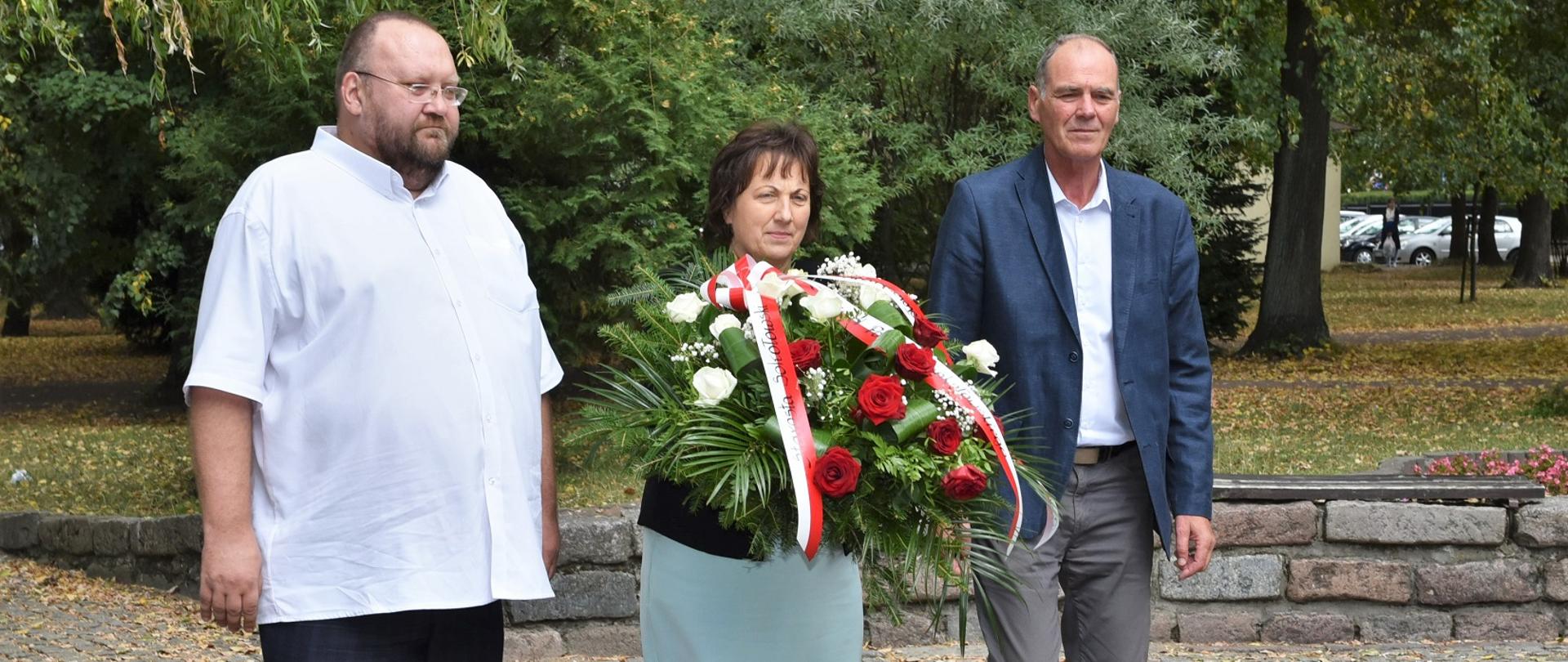 Delegacja Powiatu Sokołowskiego zbliża się z kwiatami do pomnika Czynu Niepodległościowego w Sokołowie Podlaskim.