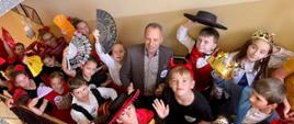 dzieci ubrane w hiszpańskie kolorowe stroje, z kapeluszami i wachlarzami pomiędzy nimi uśmiechnięty mężczyzna w garniturze 