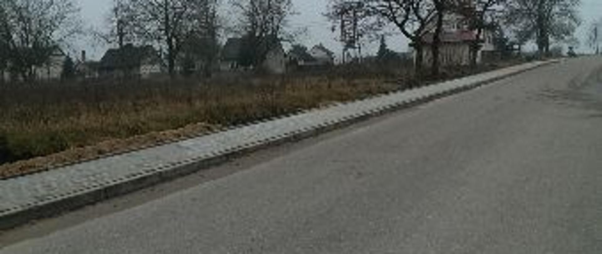 Zdjęcie przedstawia wyremontowany chodnik w Chromakowie. W tle drzewa i domy.