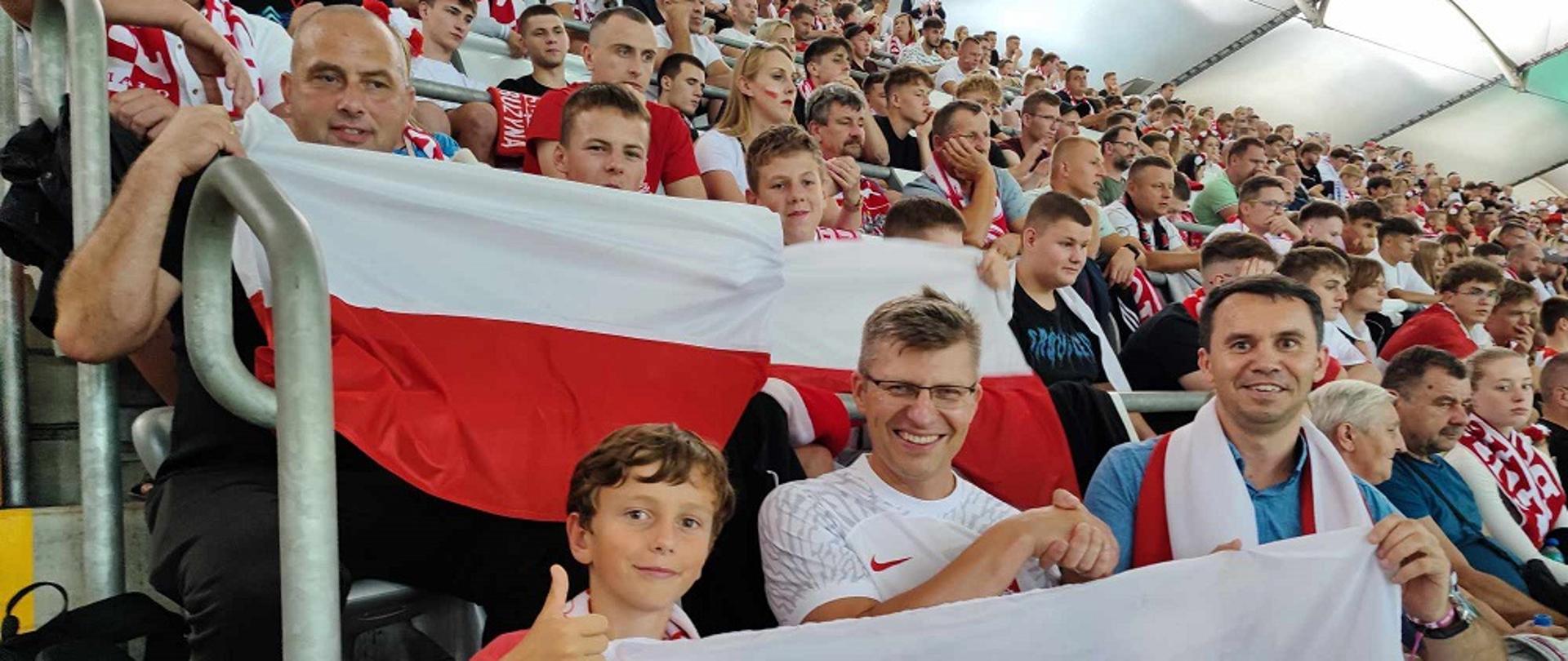kibice z flagami biało czerwonymi siedzą na trybunach stadionu 