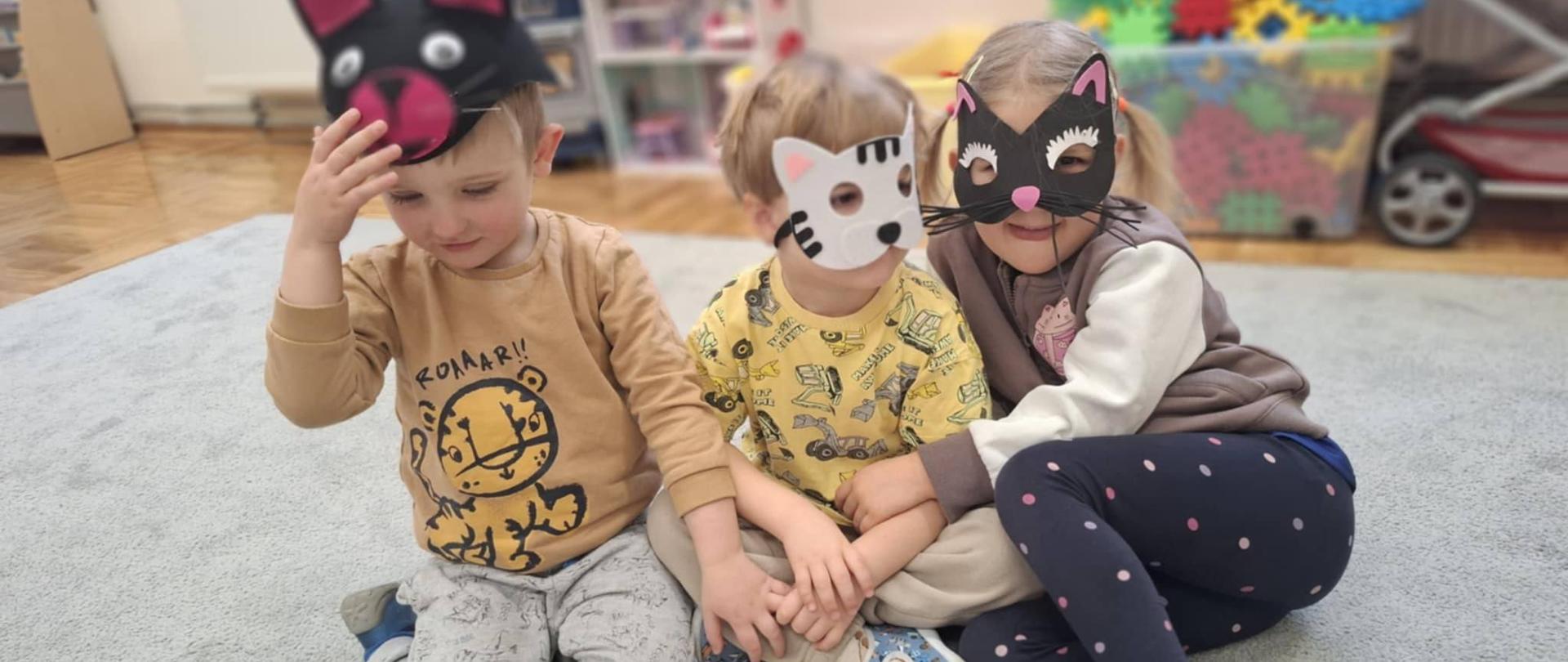 Trójka dzieci w makach kotów siedzi na dywanie.