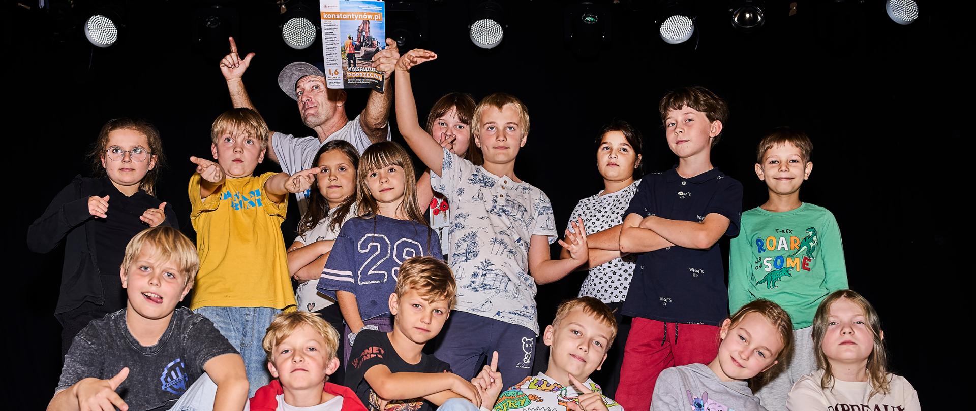 Grupa dzieci z zespołu Dynamic Beat i mężczyzna trzymający egzemplarz Informatora Miejskiego, pozujący do wspólnego zdjęcia na scenie.