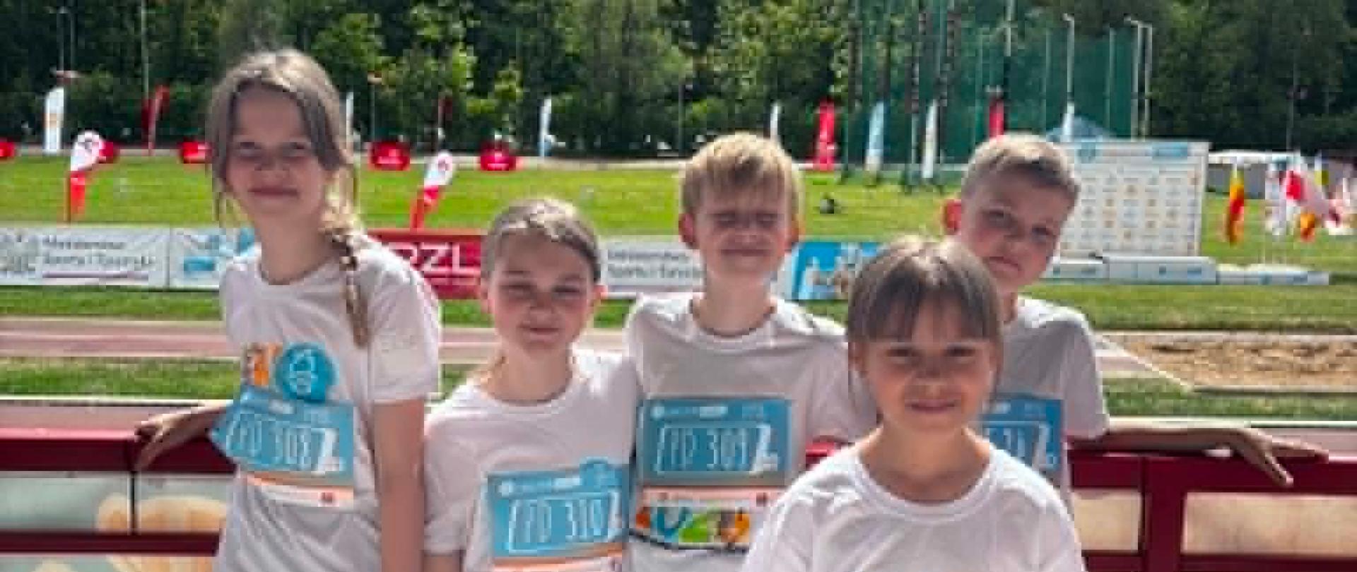 Pięcioro reprezentantów naszej szkoły w zawodach sportowych- Paulina Gosk, Antonina Moroz, Martyna Mitros, Witold Gosk oraz Gabriel Połubiński pozują do wspólnego zdjęcia. Wszyscy ubrani są w stroje sportowe.