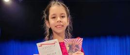 Oliwia pozuje z nagrodami - pluszowym misiem, dyplomem i statuetką