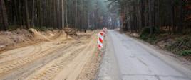 przebudowa jezdni, z lewej strony ściągnięty asfalt i wysypany piaskiem wzdłuż jezdni ostrzegawcze słupki biało czerwone 