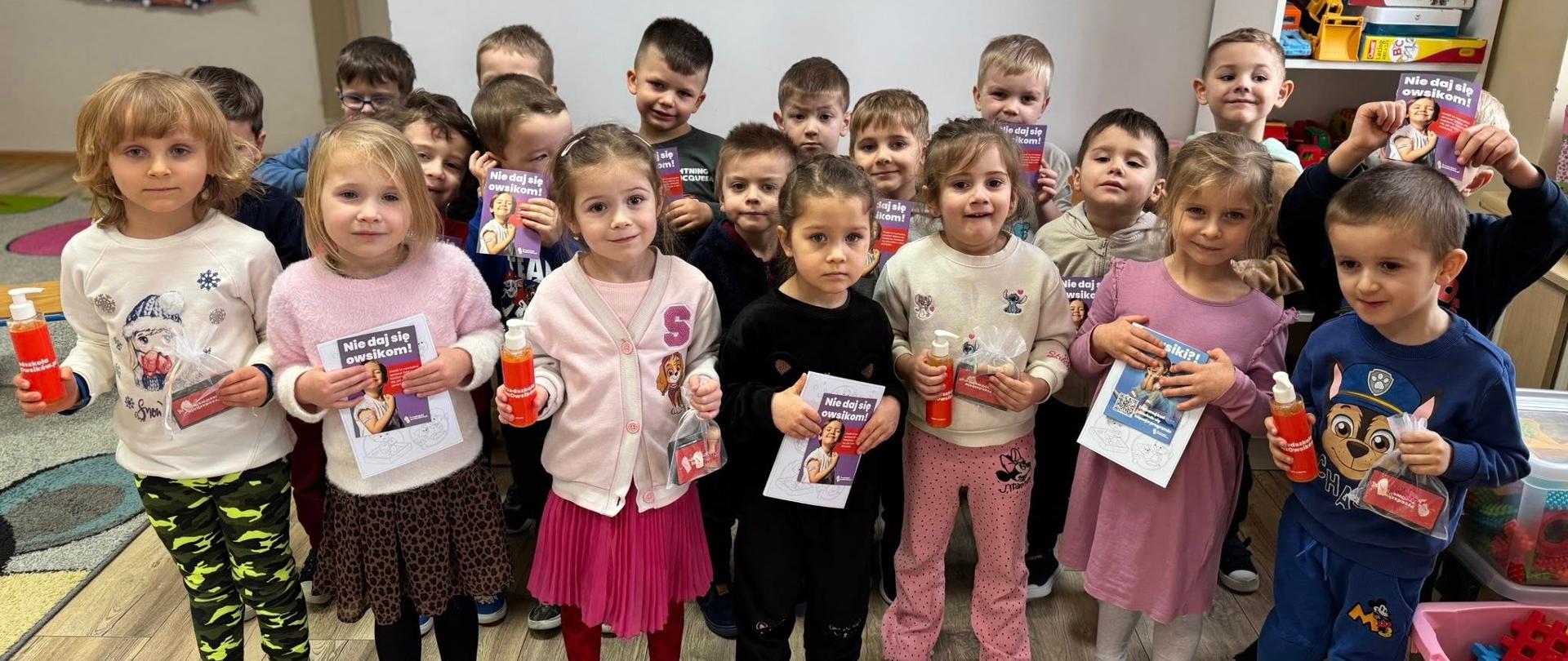 Grupa dzieci pokazuje granty otrzymane w ramach programu "Przedszkola bez owsików"