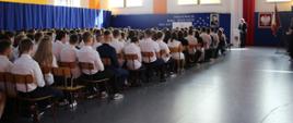 zdjęcie hali podczas rozpoczęcia roku szkolnego , znajdują się uczniowie, a w tle dyrektor ZS1 przemawia