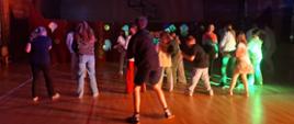 Uczniowie tańczą na spowitej mrokiem, rozświetlonej tylko światłami disco sali gimnastycznej