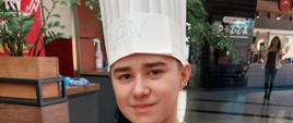 Uczeń w czapce kucharskiej trzyma pizzę