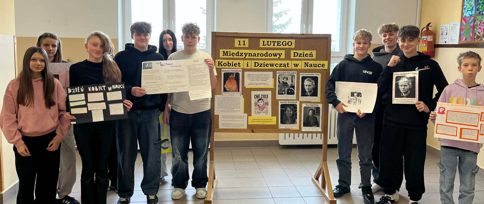 Młodzież z klasy 8 na tle gazetki szkolnej prezentuje swoje plakaty