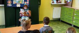 Dziewczynka na krześle czyta książkę dla pozostałych uczniów w klasie