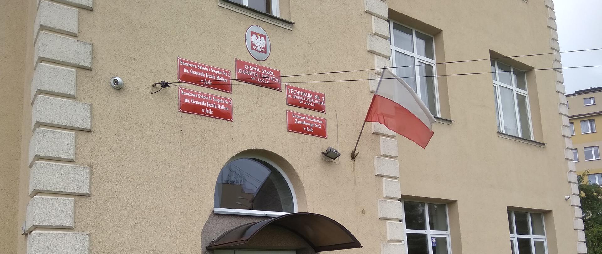 Budynek A Zespołu Szkół Usługowych i Spożywczych w Jaśle. Na zdjęciu front budynku szkoły z wejściem głównym i tablicami informacyjnymi.