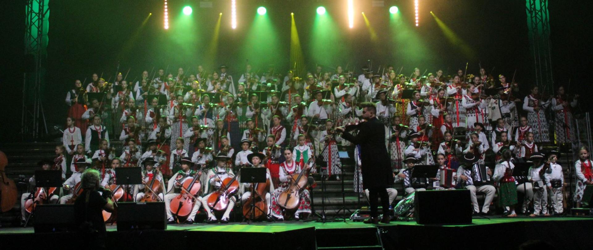 Zdjęcie zespołu Małej Armii Janosika. Na oświetlonej scenie ponad 150 wykonawców w strojach góralskich.