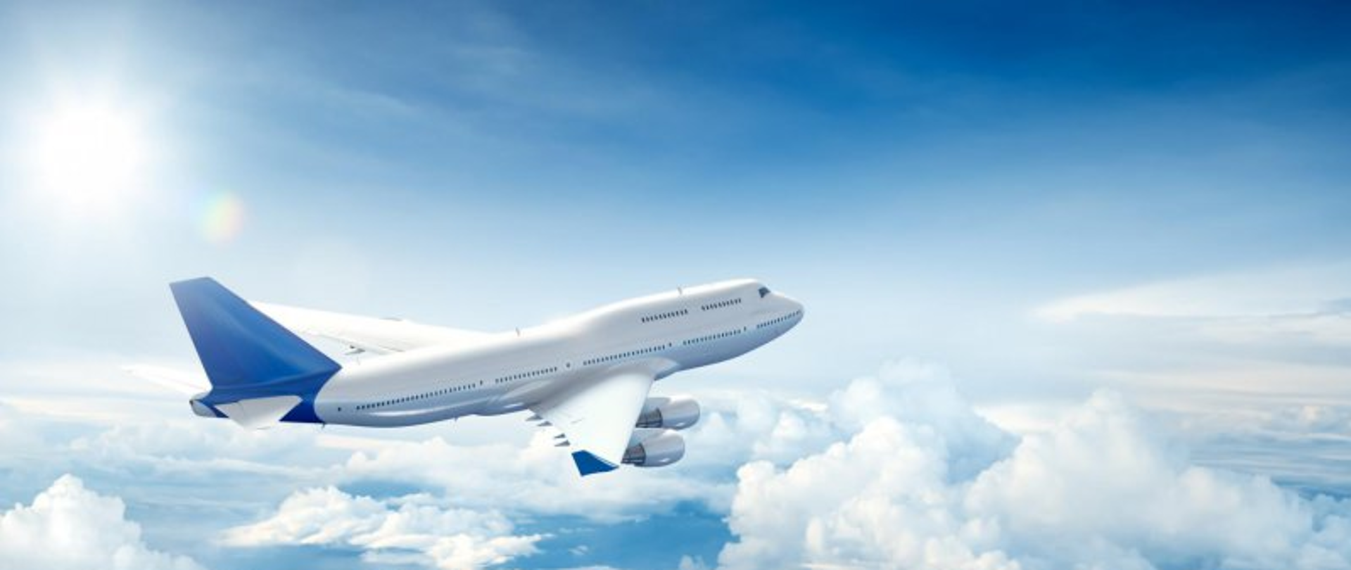 Grafika przedstawia: biały samolot pasażerski lecący w chmurach na tle błękitnego nieba