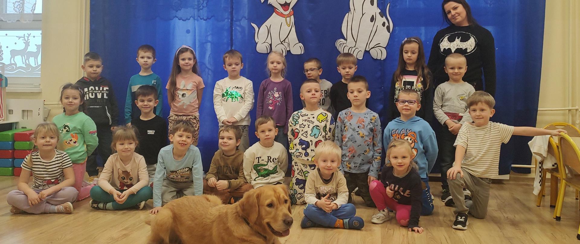 Wspólne zdjęcie przedszkolaków z panią Kasią oraz leżącym przed nimi psem Miku rasy Golden Retriever.