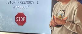 Prowadzący warsztaty stoi obok monitora interaktywnego, na którym widnieje napis "Stop agresji i przemocy"